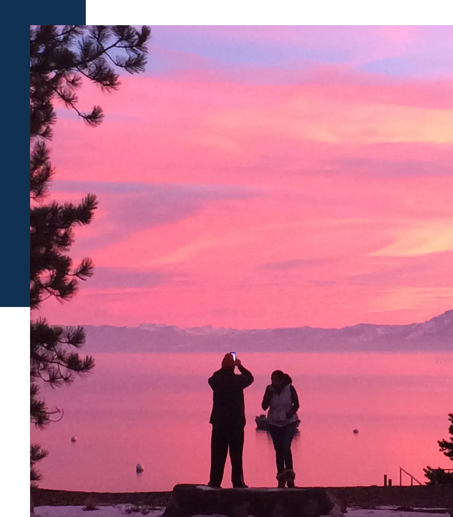 Two people standing on a beach looking at the sunset.